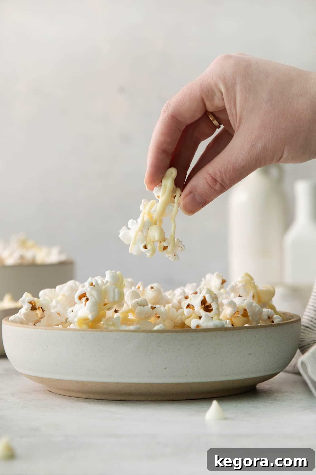Gourmet White Chocolate Pop 7 White chocolate popcorn in a bowl with a hand reaching for a piece