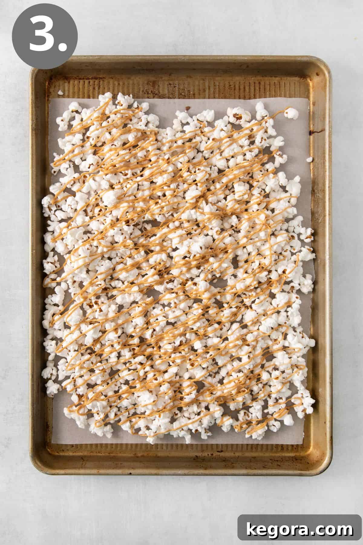Nutty Caramel Popcorn 6 Peanut butter drizzle being applied over popcorn spread on a sheet pan