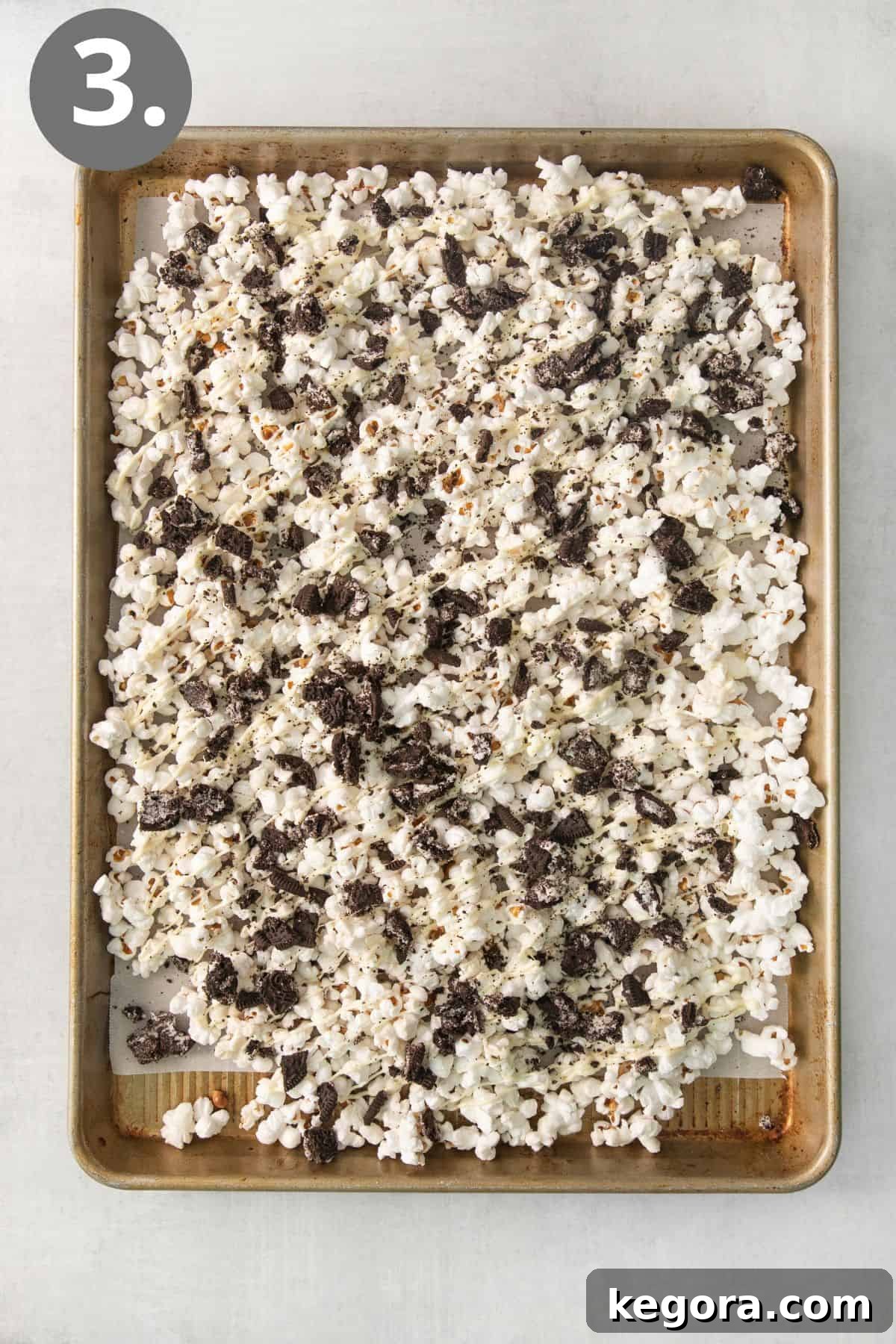 Cookies and Cream Popcorn 6 Freshly popped Oreo popcorn spread out on a baking tray, glistening with white chocolate and cookie pieces.
