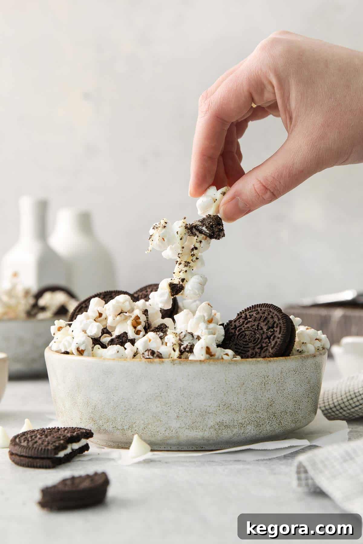 Cookies and Cream Popcorn 7 A hand reaching into a bowl of freshly made Oreo popcorn to grab a delicious piece.