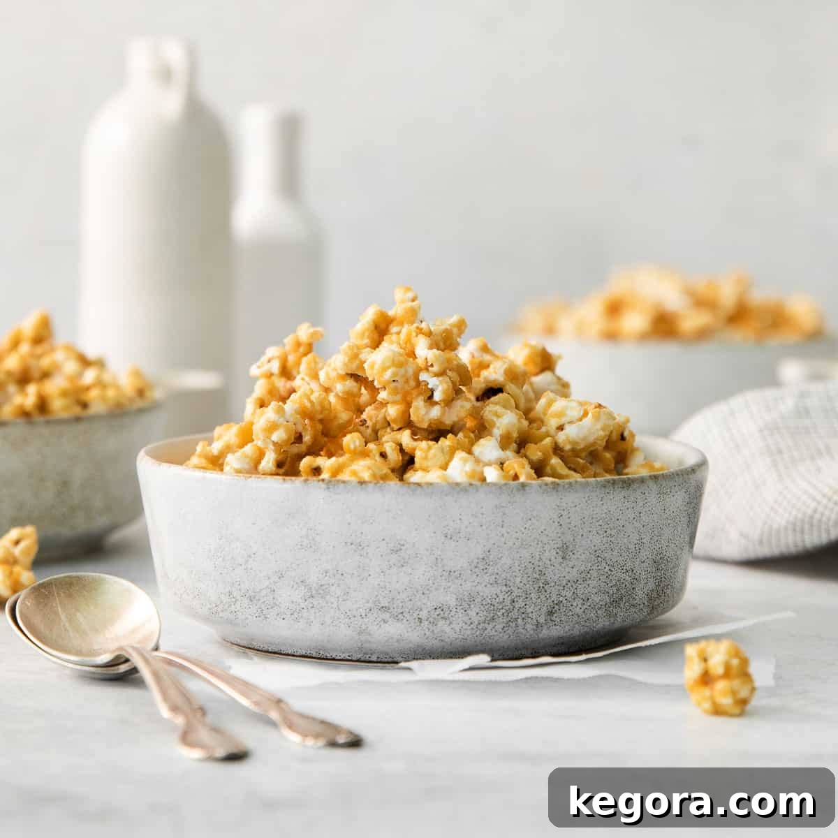 Effortless Caramel Popcorn Treat 9 Microwave caramel corn in a bowl on a countertop, with bowls of popcorn and jars of milk in the background