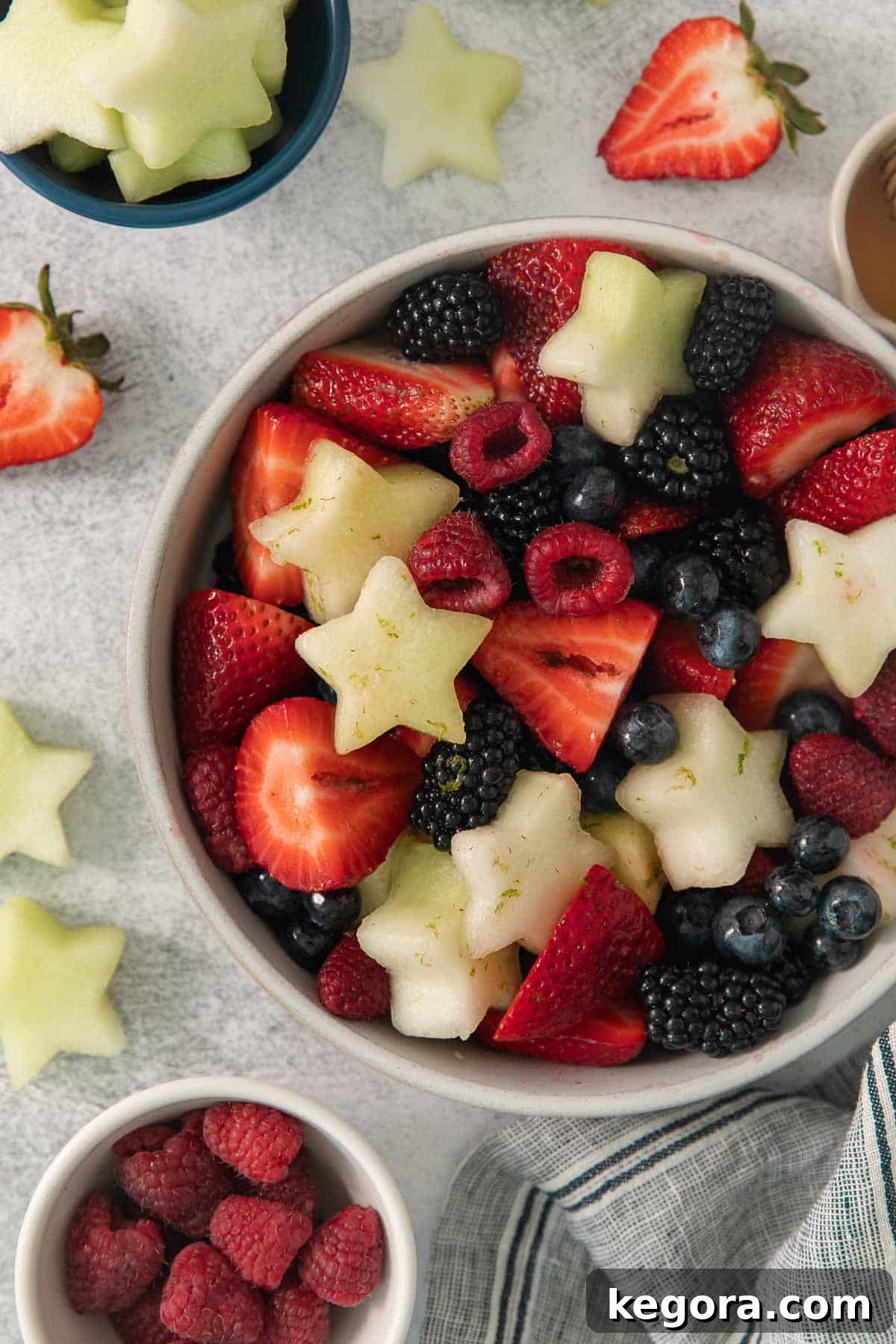Red White and Blue Fruit Celebration 2 A beautifully arranged 4th of July fruit salad in a large glass bowl, surrounded by fresh whole berries and melon slices.