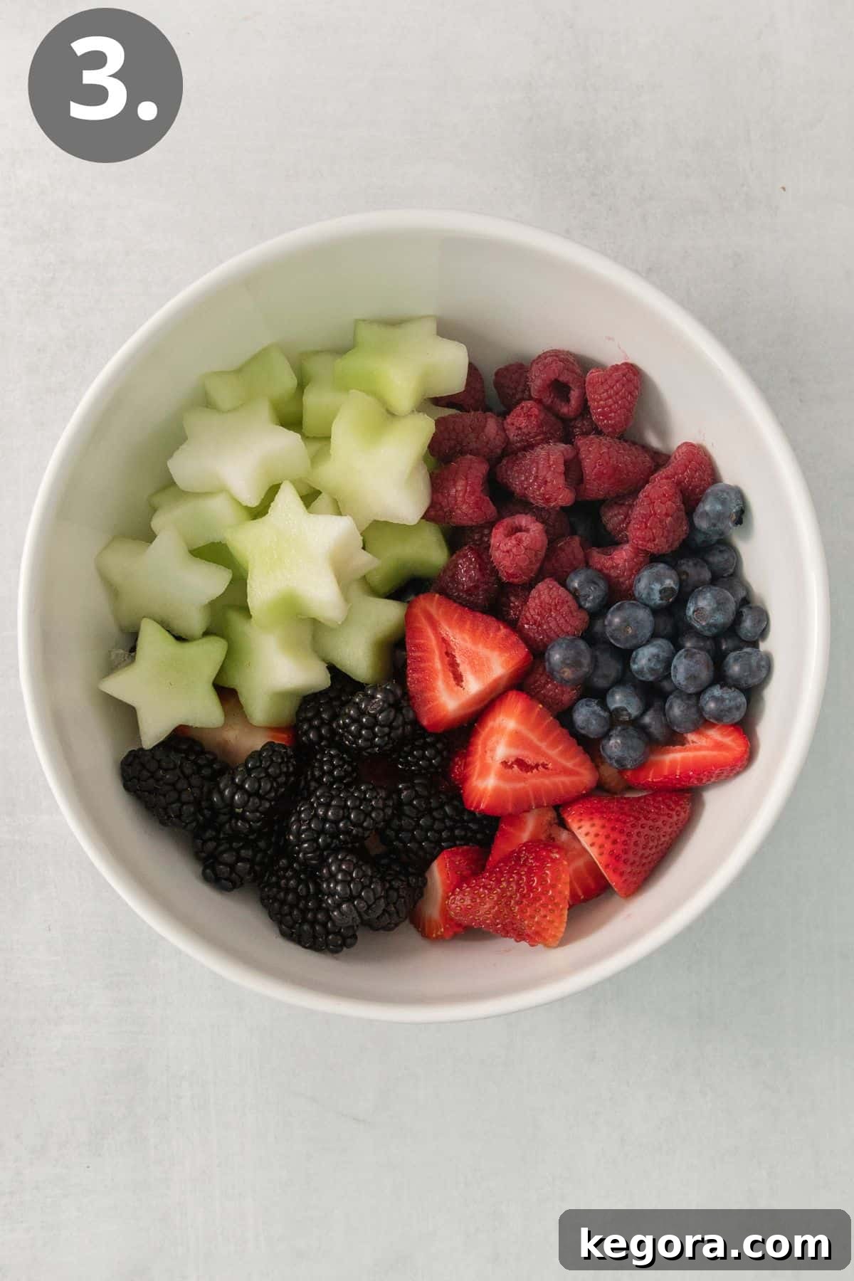 Red White and Blue Fruit Celebration 6 A large serving bowl filled with a colorful mix of honeydew stars, sliced strawberries, blueberries, raspberries, and blackberries, before dressing.