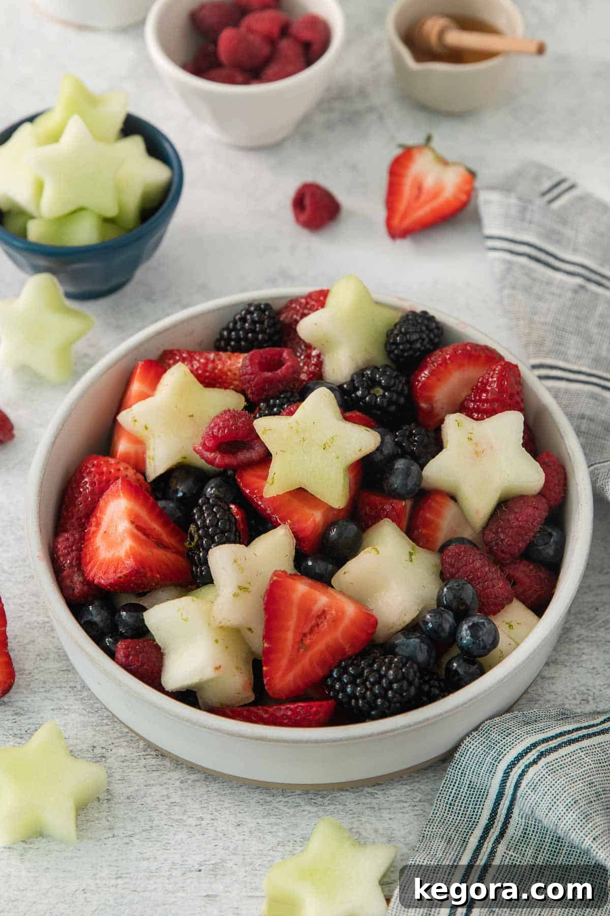 Red White and Blue Fruit Celebration 8 Side angle shot of a vibrant Fourth of July fruit salad in a large glass bowl, with a scattering of fresh berries and melon slices around it.