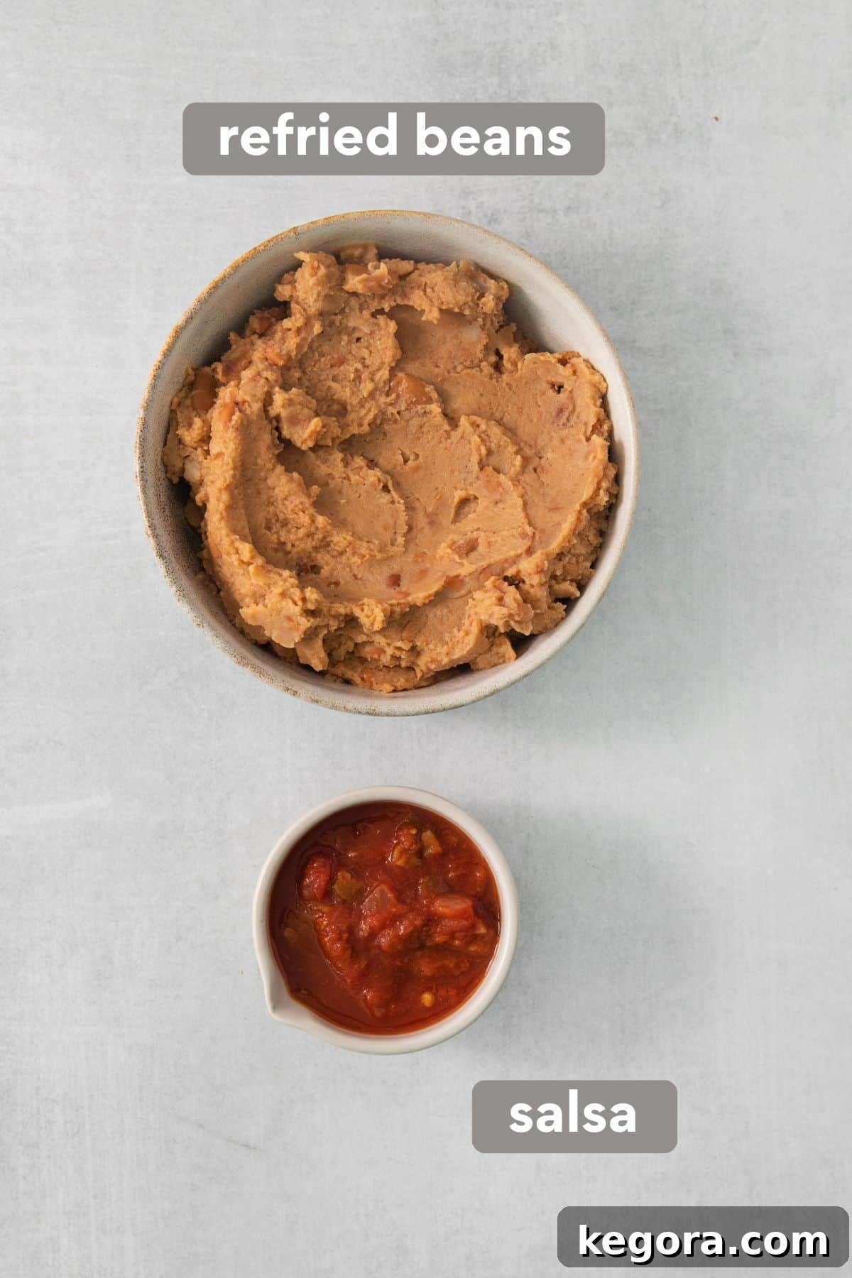 Two cans of refried beans and a bowl of vibrant red salsa, ready to be combined for the foundational layer of a 7-layer taco dip.
