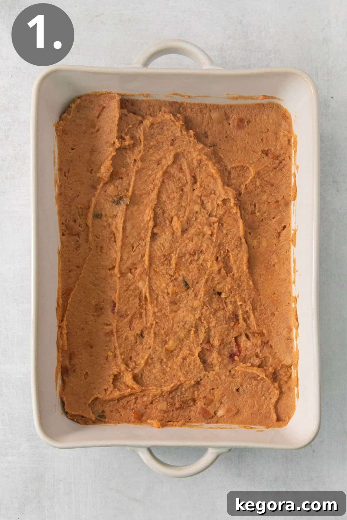 The first layer of refried beans and salsa, smoothly spread across the bottom of a 9x13-inch baking dish, ready for the next layer.