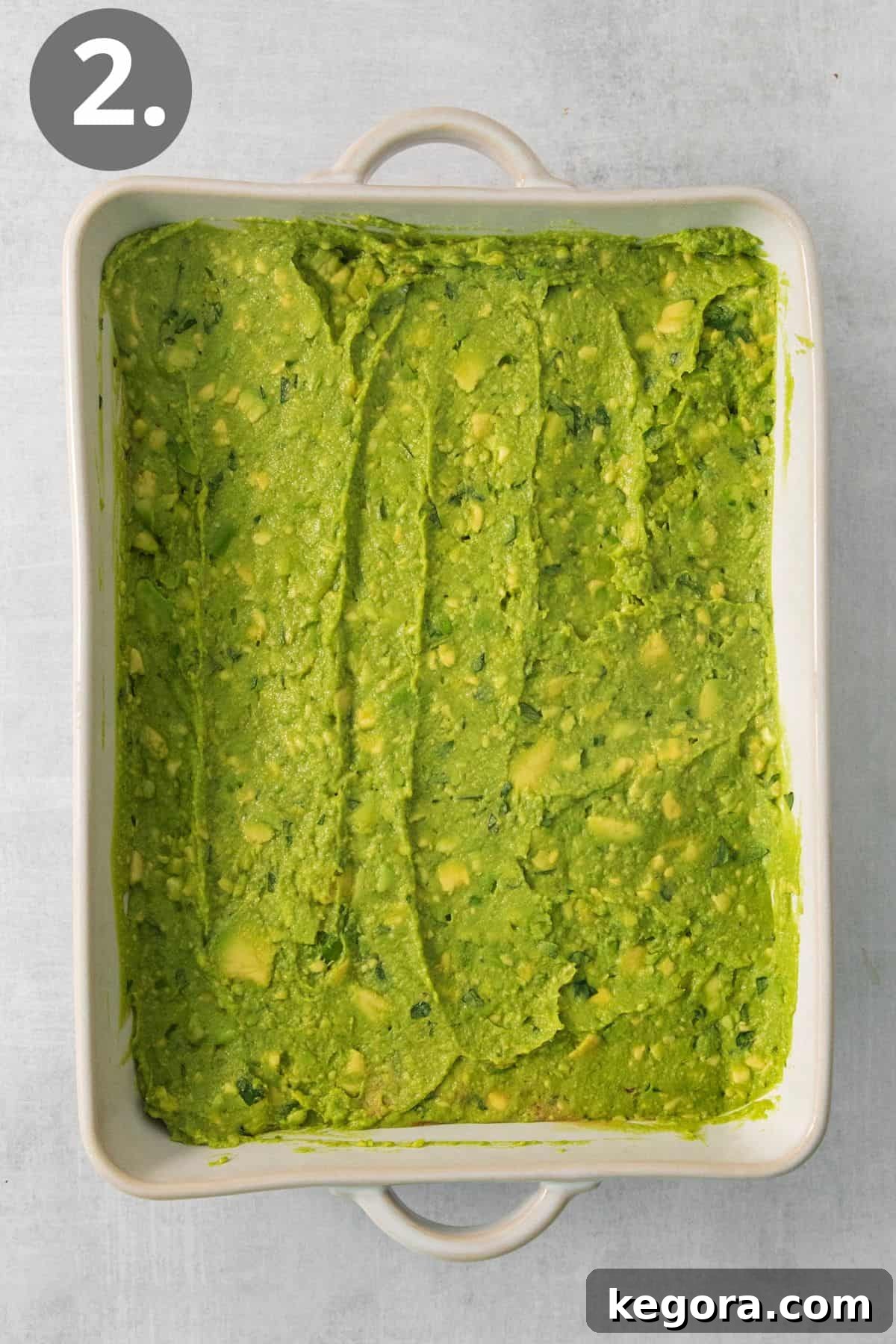 The vibrant green guacamole layer smoothly spread over the refried beans in a baking dish, forming the second distinct layer of the dip.