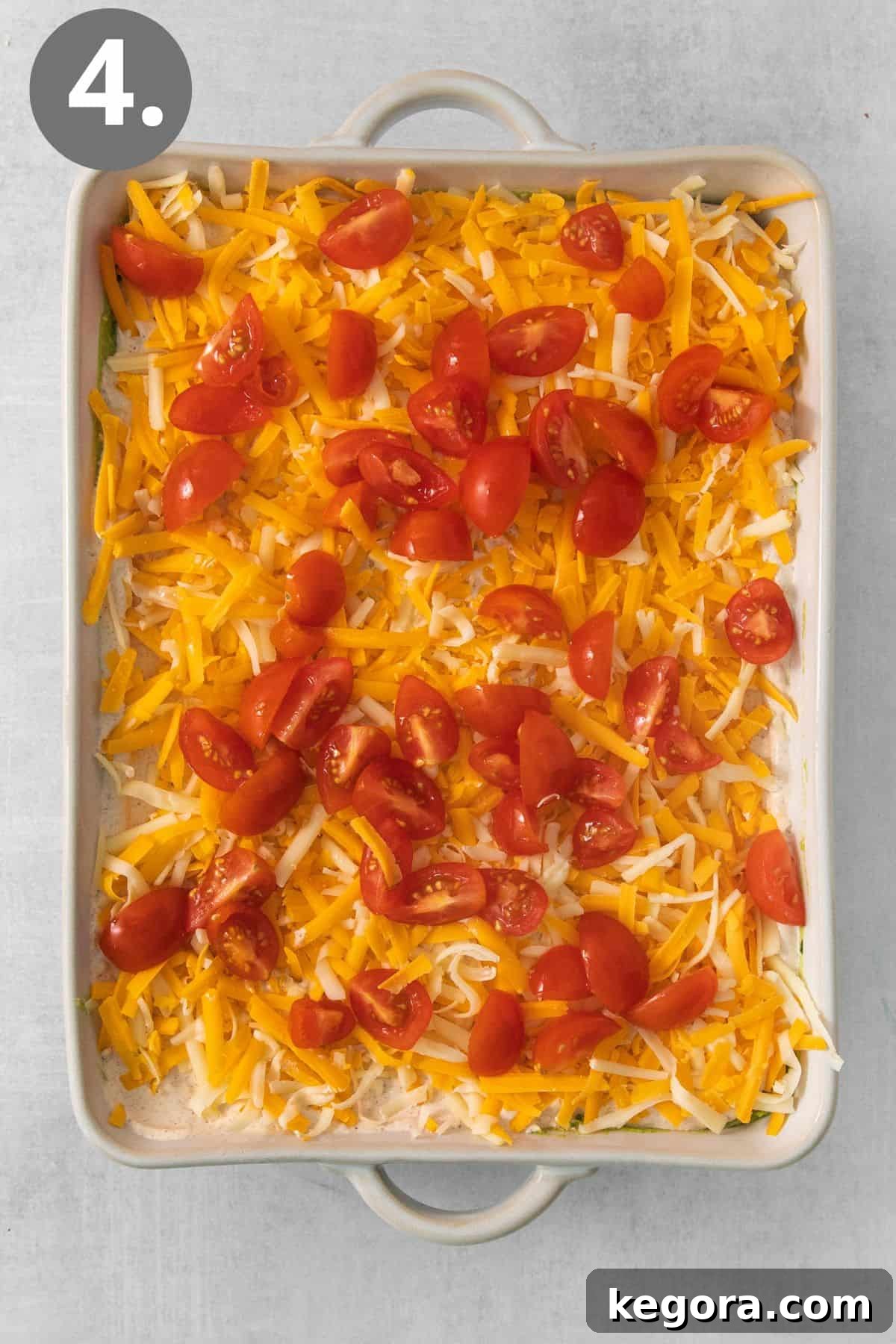 The final layers of shredded cheese and diced tomatoes artfully sprinkled over the sour cream base of the 7-layer taco dip.