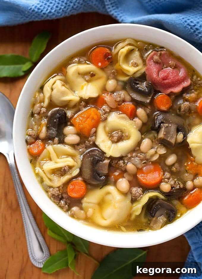 Effortless Instant Pot Mini Tortellini Soup 2 A vibrant bowl of Instant Pot Tortellini Soup, garnished with fresh herbs and served on a wooden board with a spoon, highlighting its creamy texture and rich ingredients.