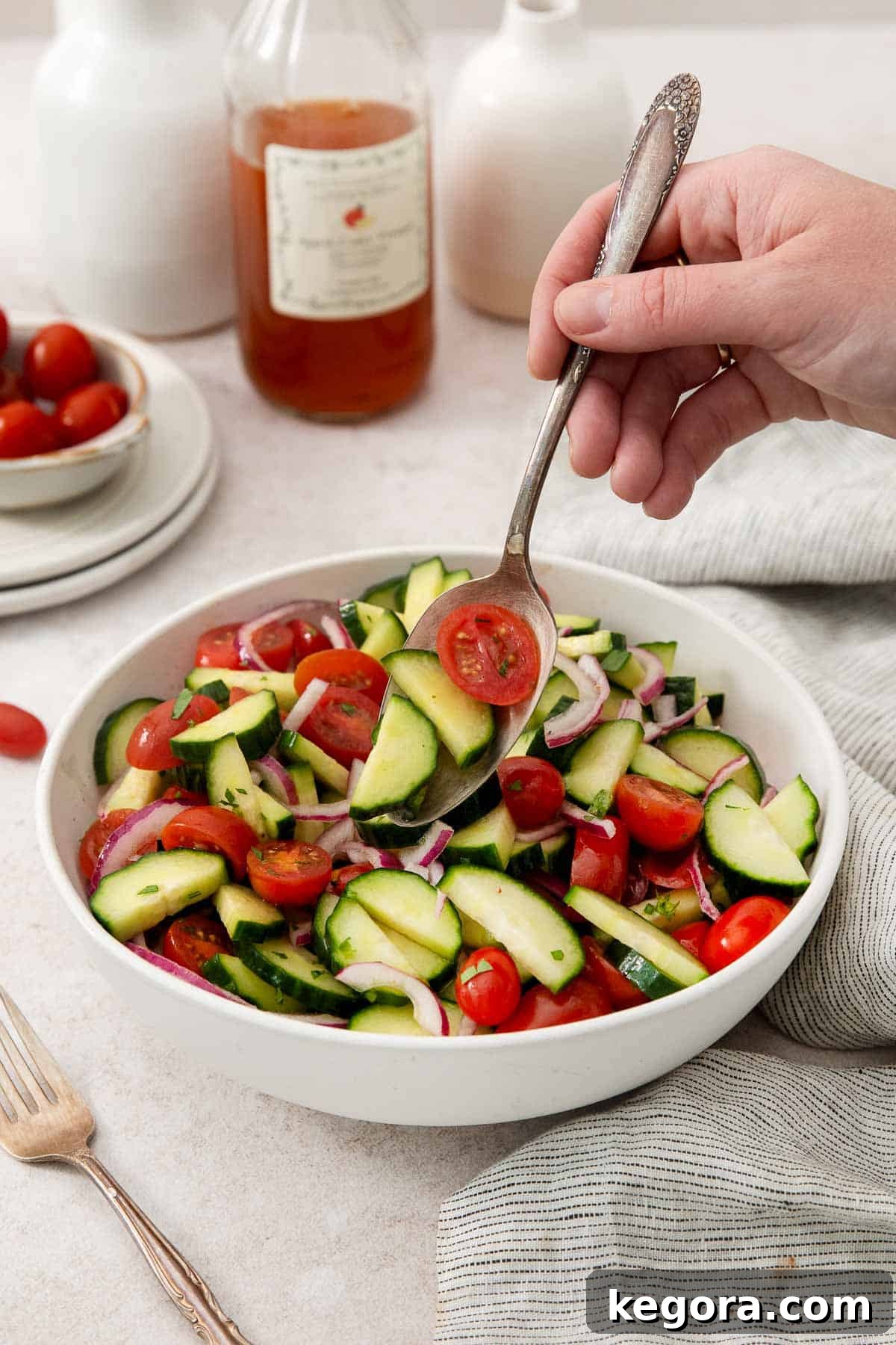 Easy Tangy Cucumber Tomato Salad 6 A close-up shot of Marinated Cucumber Tomato Salad in a serving bowl, with a hand reaching in with a fork, emphasizing its irresistible freshness and readiness to be enjoyed.