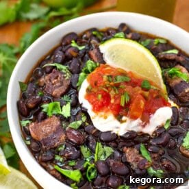 Perfect Black Beans from Your Instant Pot Mini 4 Black Beans in a white bowl on a wooden board garnished with lime wedge and cilantro