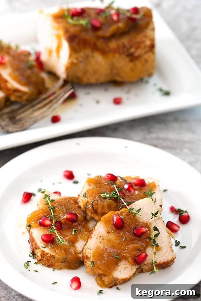 Sliced Balsamic Apple Pork Tenderloin garnished with pomegranate and thyme on a white plate