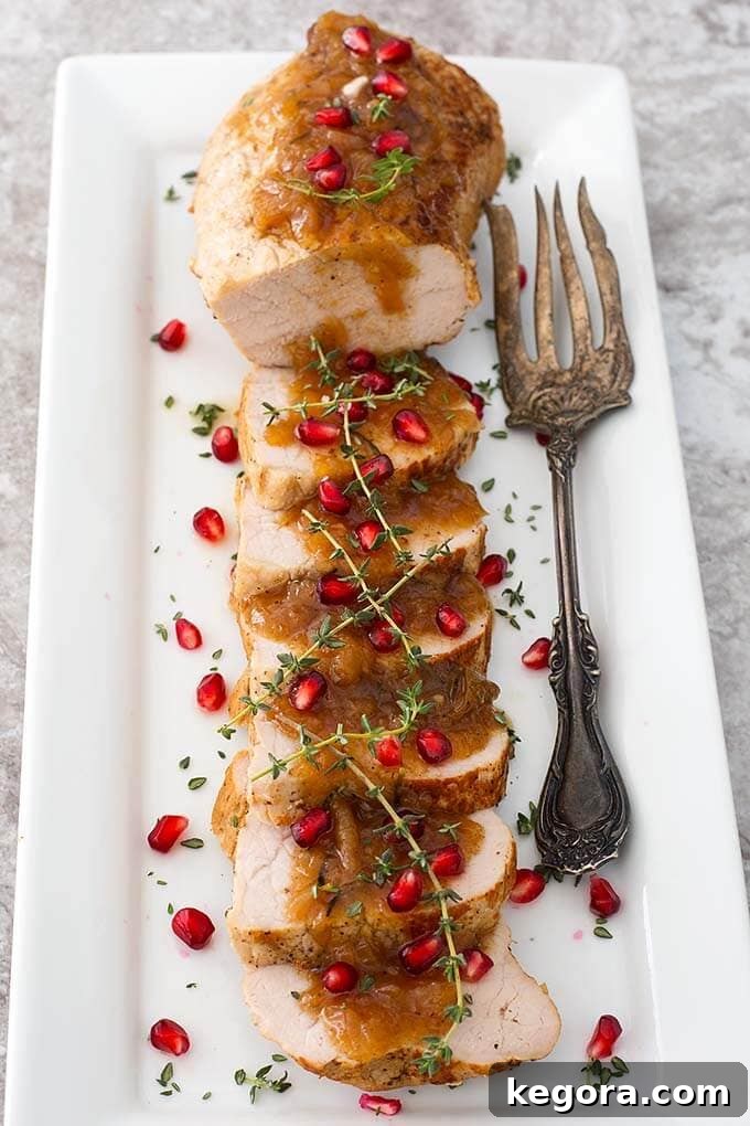 Sliced Balsamic Apple Pork Tenderloin Balsamic Apple Pork Tenderloin garnished with pomegranate and thyme on a white plate