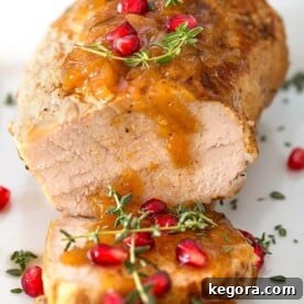 Balsamic Apple Pork Tenderloin garnished with pomegranate and thyme on a white plate