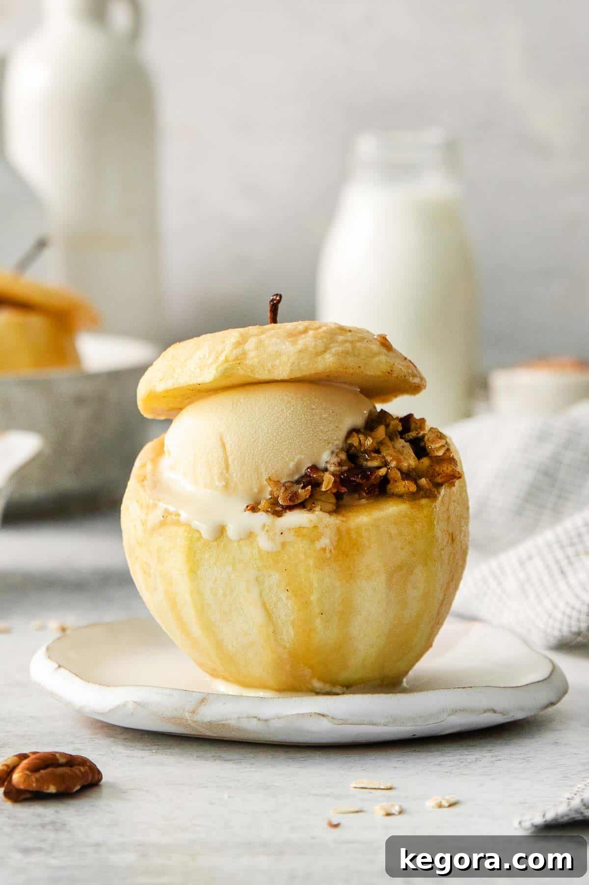 Comforting Gluten-Free Baked Apples 3 A baked apple with golden filling, topped with a scoop of melting vanilla ice cream and maple drizzle on a white plate with a fork.