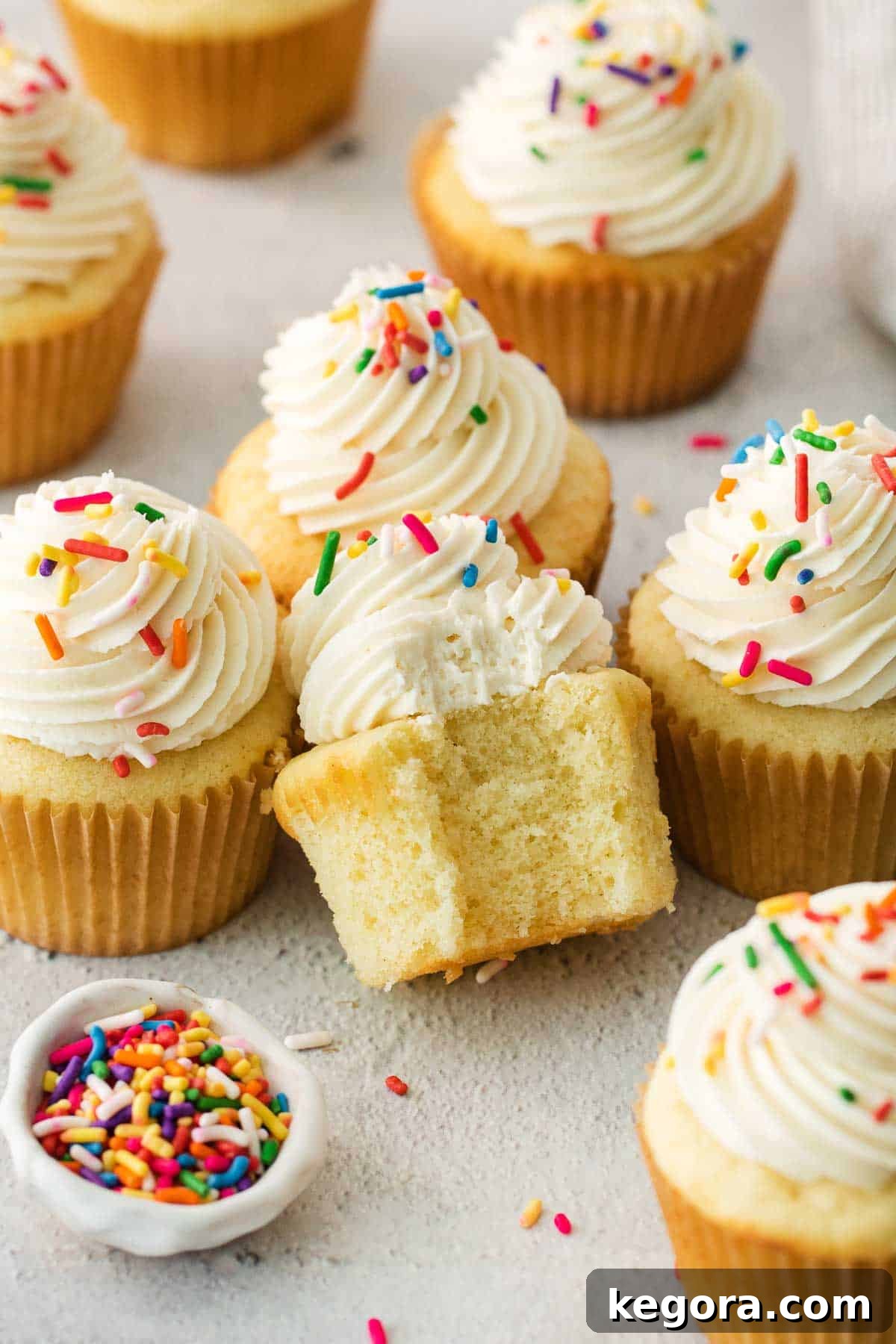 Two beautifully frosted gluten-free vanilla cupcakes, one with a bite taken out, adorned with colorful sprinkles.