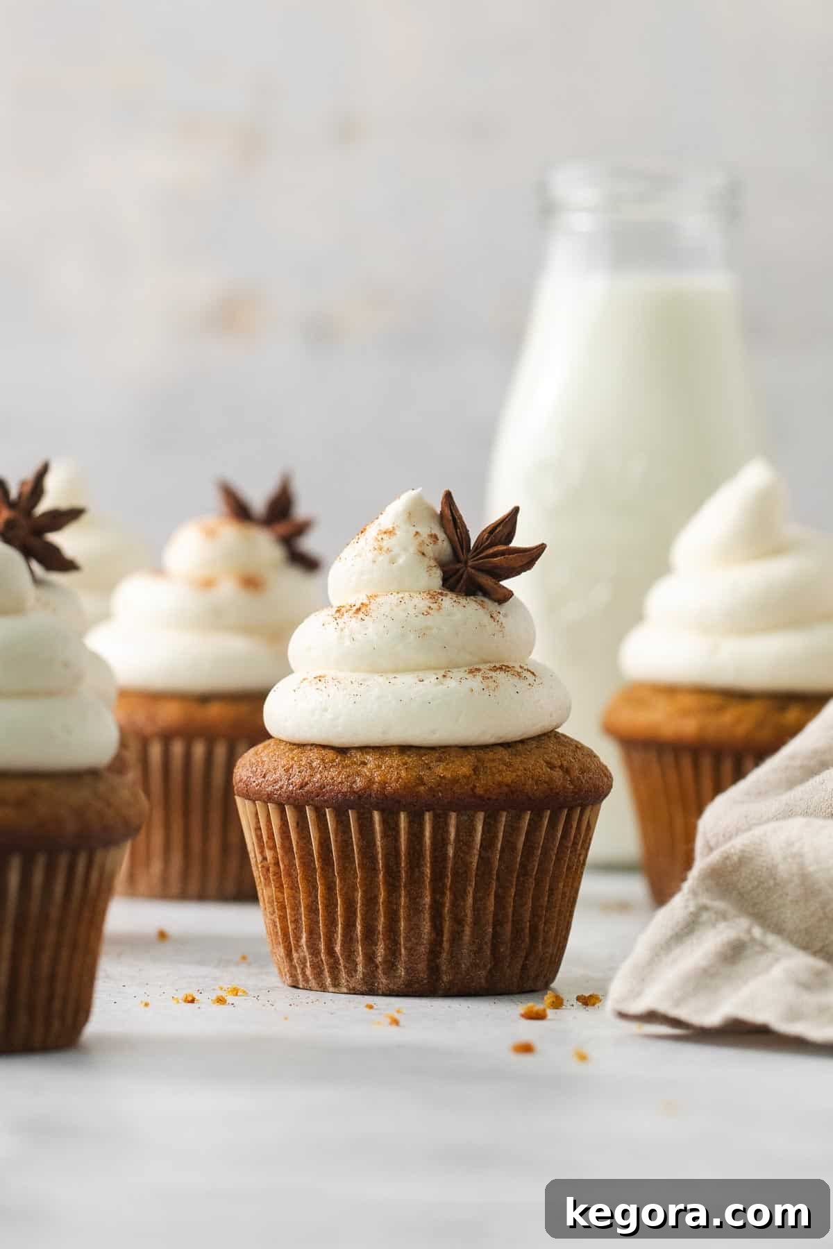 Gluten-free pumpkin cupcakes on a countertop with milk in the background, showcasing their perfect frosting and inviting color.