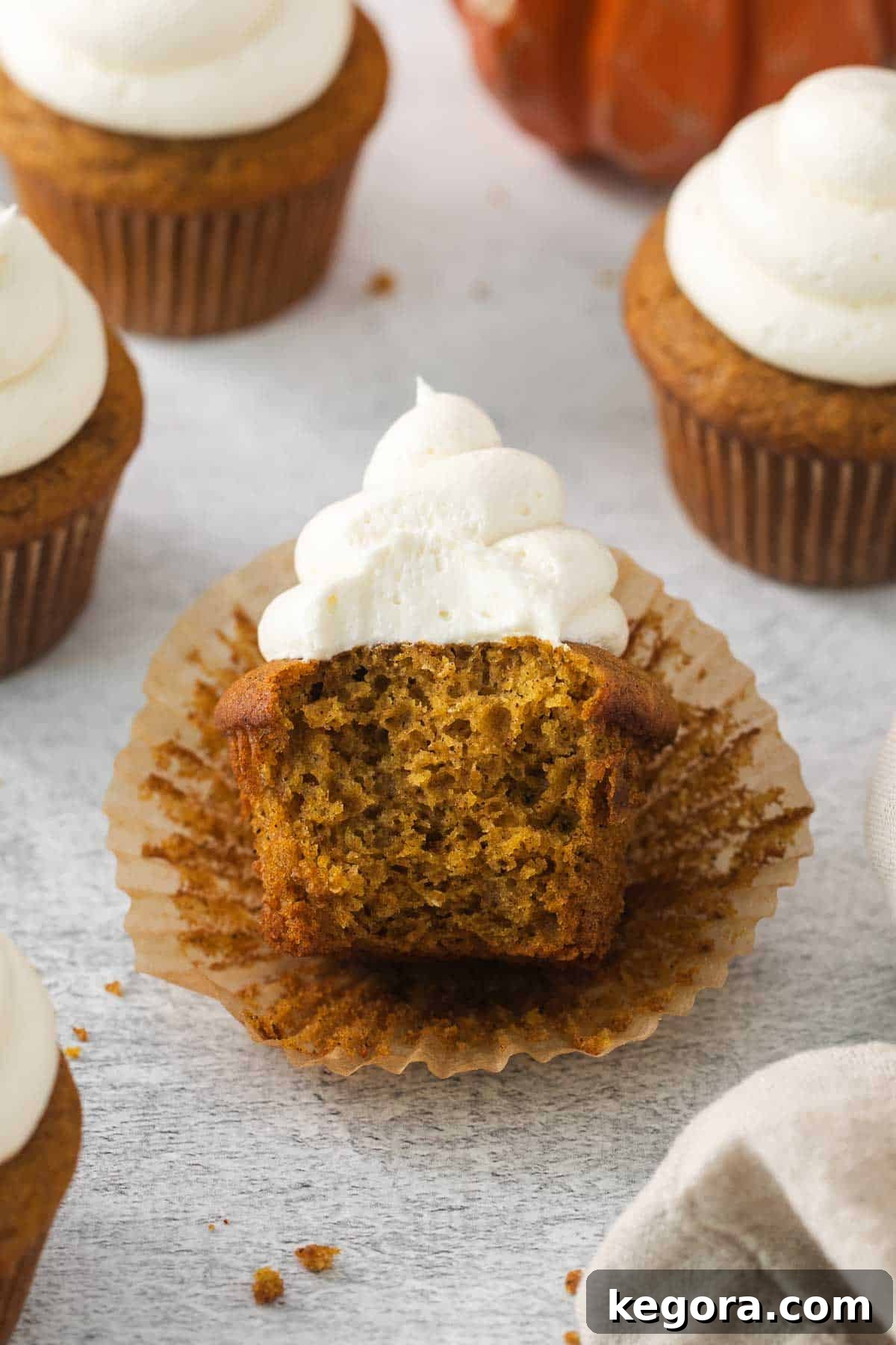 A perfectly frosted gluten-free pumpkin cupcake with a bite taken out of it, revealing its moist and tender interior.