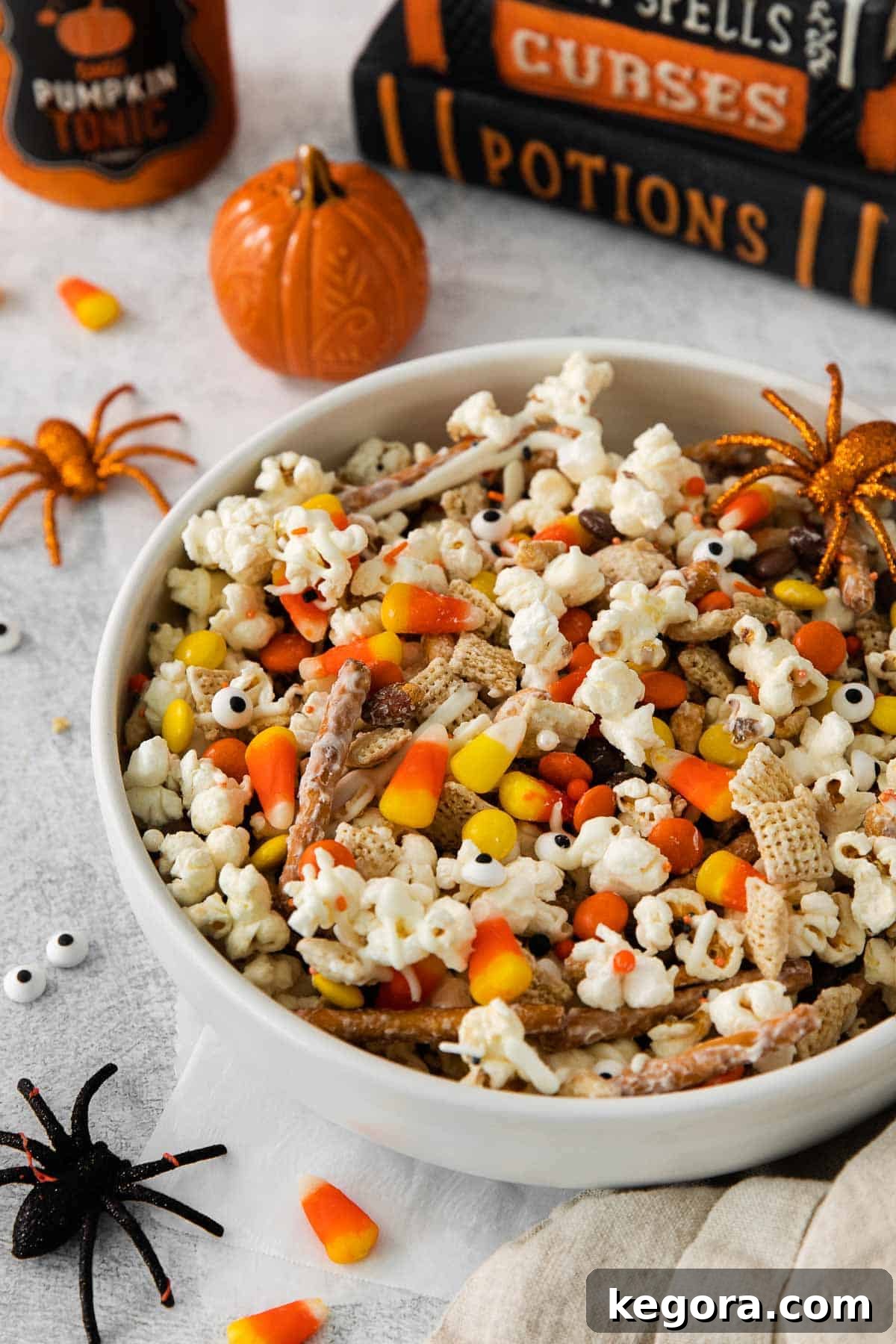 Monster Munch Mix 2 A bowl brimming with vibrant Halloween snack mix, featuring popcorn, pretzels, candies, and white chocolate drizzle, set against a festive backdrop.