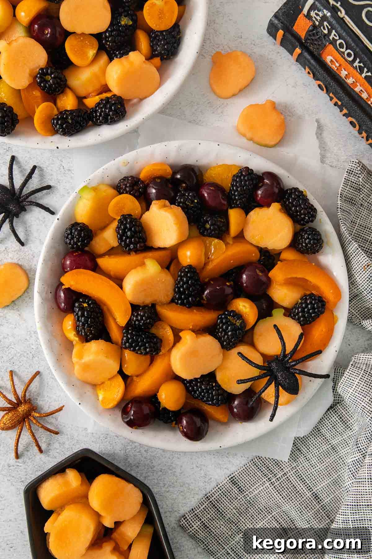 Monster Mash Fruit Salad 2 An overhead view of Halloween fruit salad in a bowl, showcasing vibrant orange and dark fruits with mini cantaloupe pumpkins.