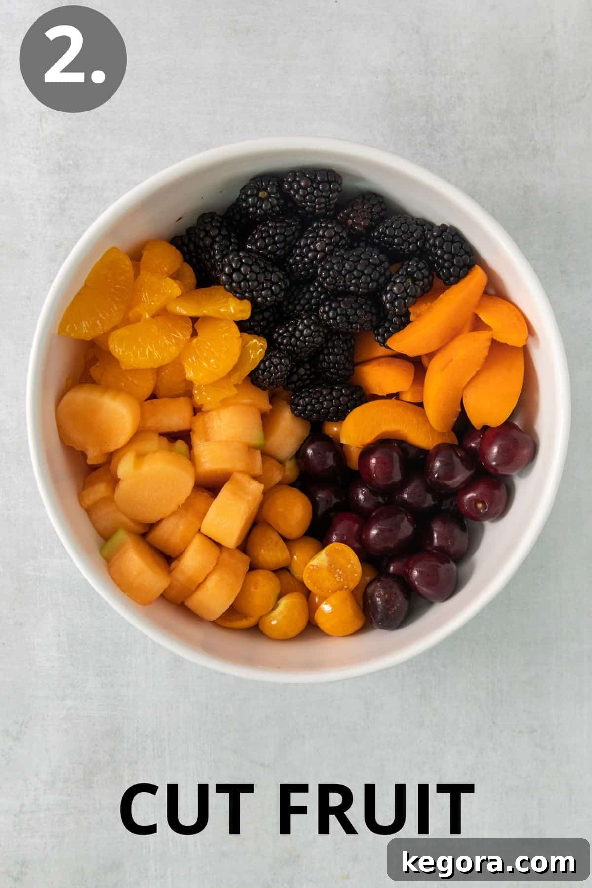 Monster Mash Fruit Salad 5 Various chopped fruits, including cantaloupe pumpkins, blackberries, and oranges, being poured into a large mixing bowl to create the Halloween fruit salad.
