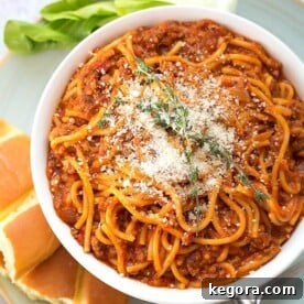Spaghetti in a white bowl on plate with bread fork and green vegetable