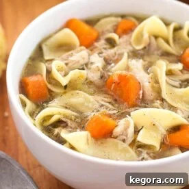 A white bowl filled with Instant Pot Mini Game Hen Noodle Soup, garnished with fresh parsley, sitting on a wooden board. This image is optimized for Pinterest.