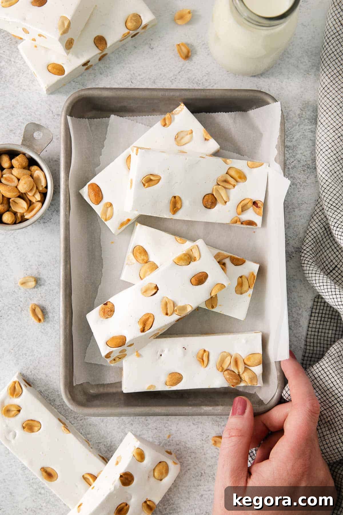 Crafting Irresistible Nougat 9 A hand gently touching a batch of homemade nougat on a parchment-lined baking sheet, showcasing its texture.