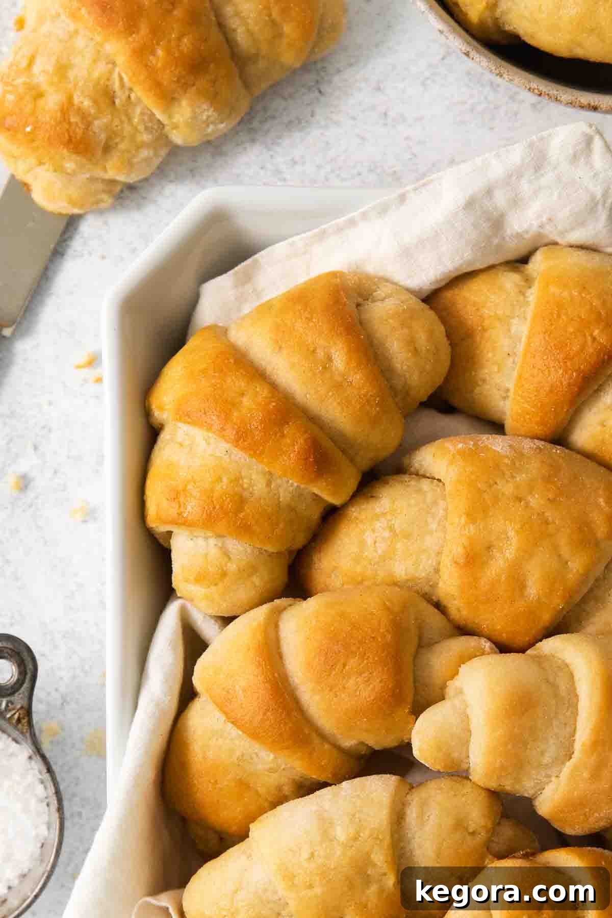 Scrumptious Gluten Free Crescent Rolls 2 Golden brown gluten-free crescent rolls arranged beautifully in a rustic bowl, with a soft kitchen towel draped nearby.