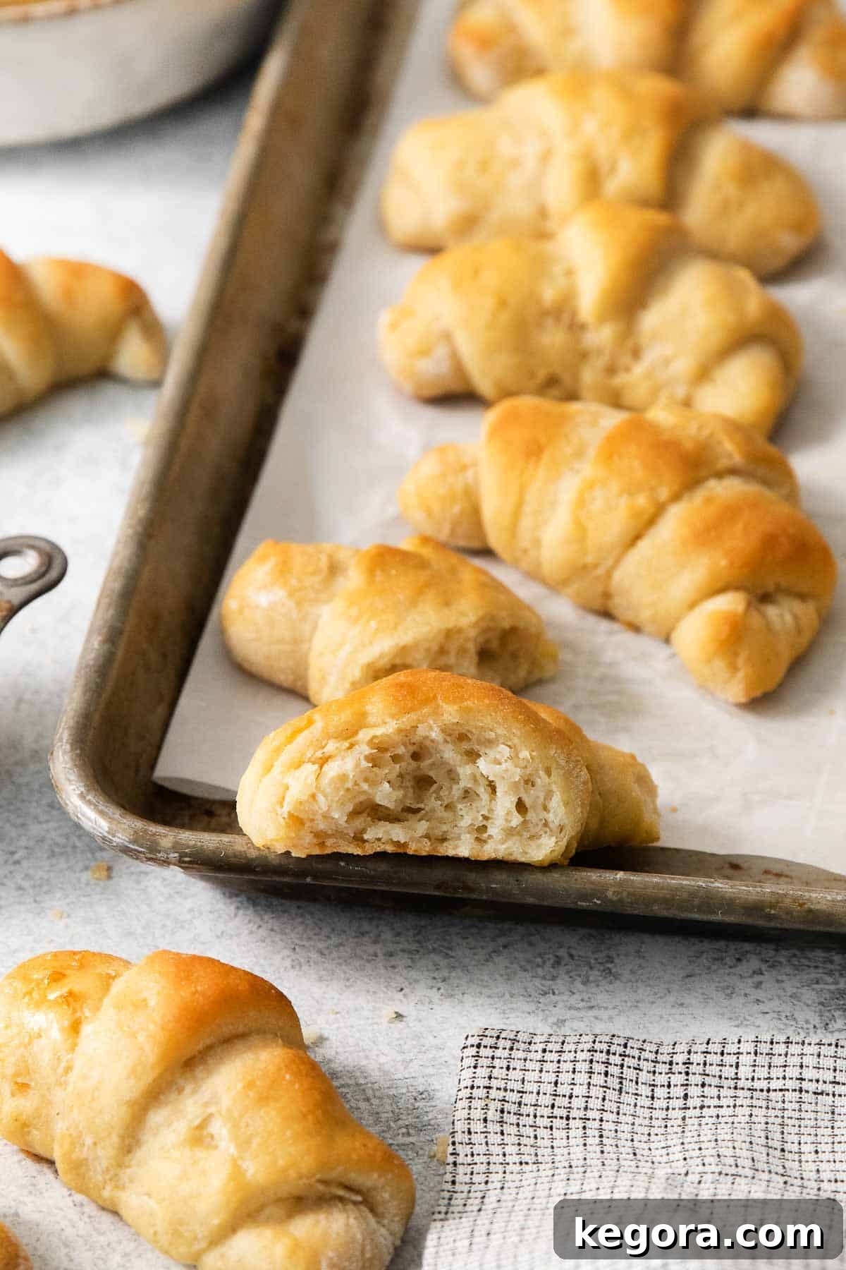 Scrumptious Gluten Free Crescent Rolls 13 A baking sheet filled with perfectly baked gluten-free crescent rolls, with one roll showing a bite taken out, highlighting its soft interior.