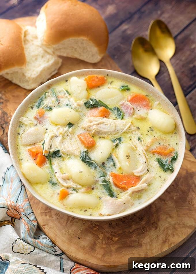 Creamy Chicken Gnocchi Soup on a wooden board with two rolls next to two golden spoons, invitingly presented