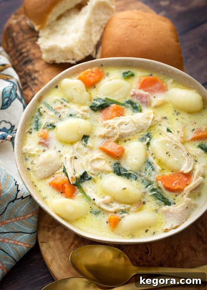 Creamy Chicken Gnocchi Soup on a wooden board with two rolls next to two golden spoons, ready to be served