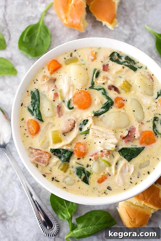 Creamy Chicken Gnocchi Soup in a white bowl next to a silver spoon on a marble background, showcasing its rich texture