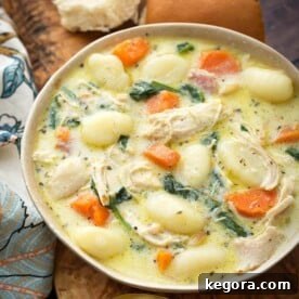 Creamy Chicken Gnocchi Soup on a wooden board with two rolls next to two golden spoons