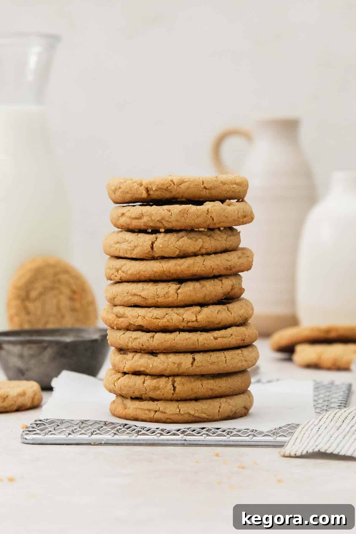 Decadent Gluten Free Peanut Butter Bites 3 A delectable stack of golden-brown gluten-free peanut butter cookies with their characteristic crinkled tops, resting on a wire cooling rack. More cookies are blurred in the background, hinting at a fresh batch.