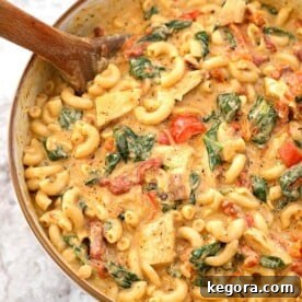 Creamy Garlic Tuscan Chicken Pasta in beige bowl with wooden spoon