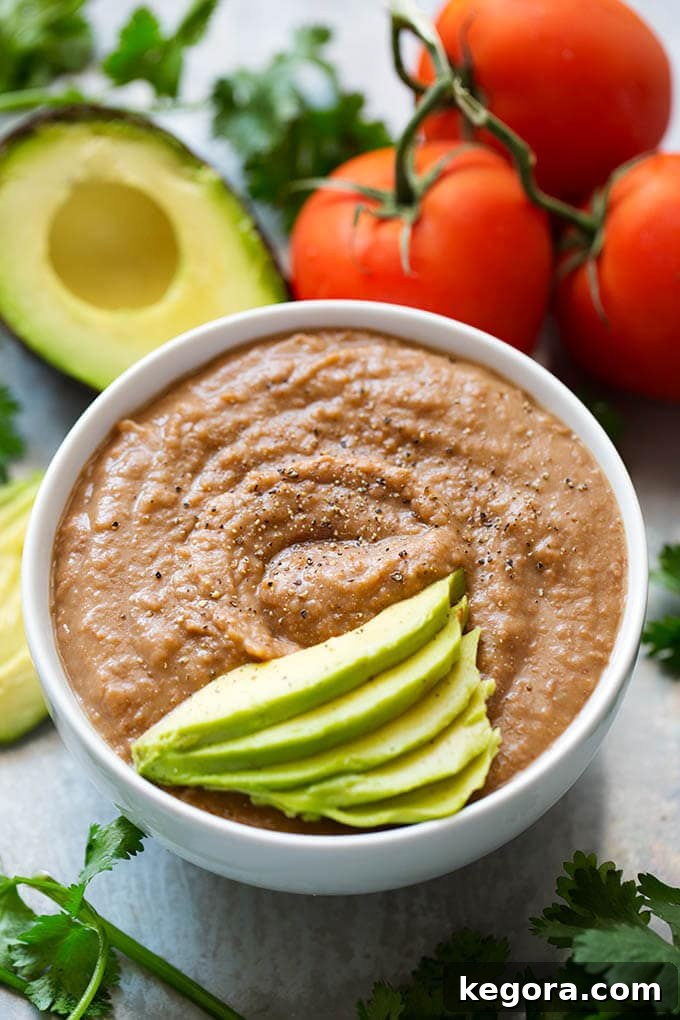 15 Instant Pot Hacks for Effortless Cooking 14 Instant Pot Refried Beans in a white bowl garnished with sliced avocado surrounded by cilantro avocado and tomatoes
