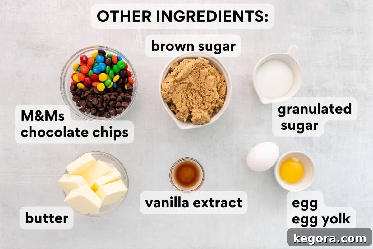 Vibrant Gluten-Free M&M Cookie Bliss 5 Wet ingredients and add-ins for gluten-free M&M cookies, including brown sugar, butter, egg, vanilla extract, and colorful M&Ms, all measured out.