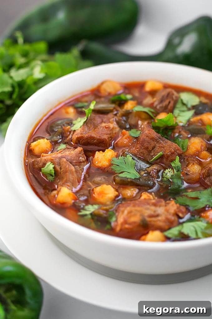 Speedy Instant Pot Pork Posole 3 A bowl of rich Instant Pot Pork Posole sits beside fresh poblano chili peppers, highlighting key ingredients.