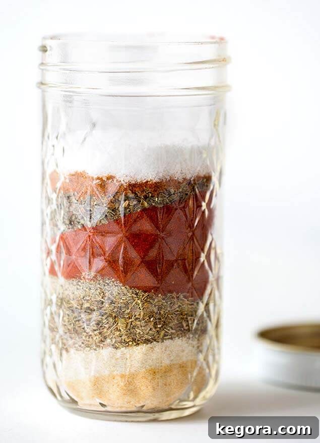A small canning jar containing a homemade layered Cajun Spice Blend, showcasing the individual spices.