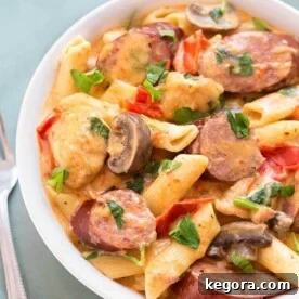 Creamy Cajun Pasta with sausage in a white bowl next to silver fork