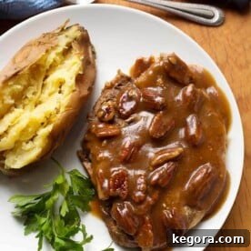 Maple Mustard Pork Chops with baked potato and parsley on a white plate on wooden board next to fork and knife