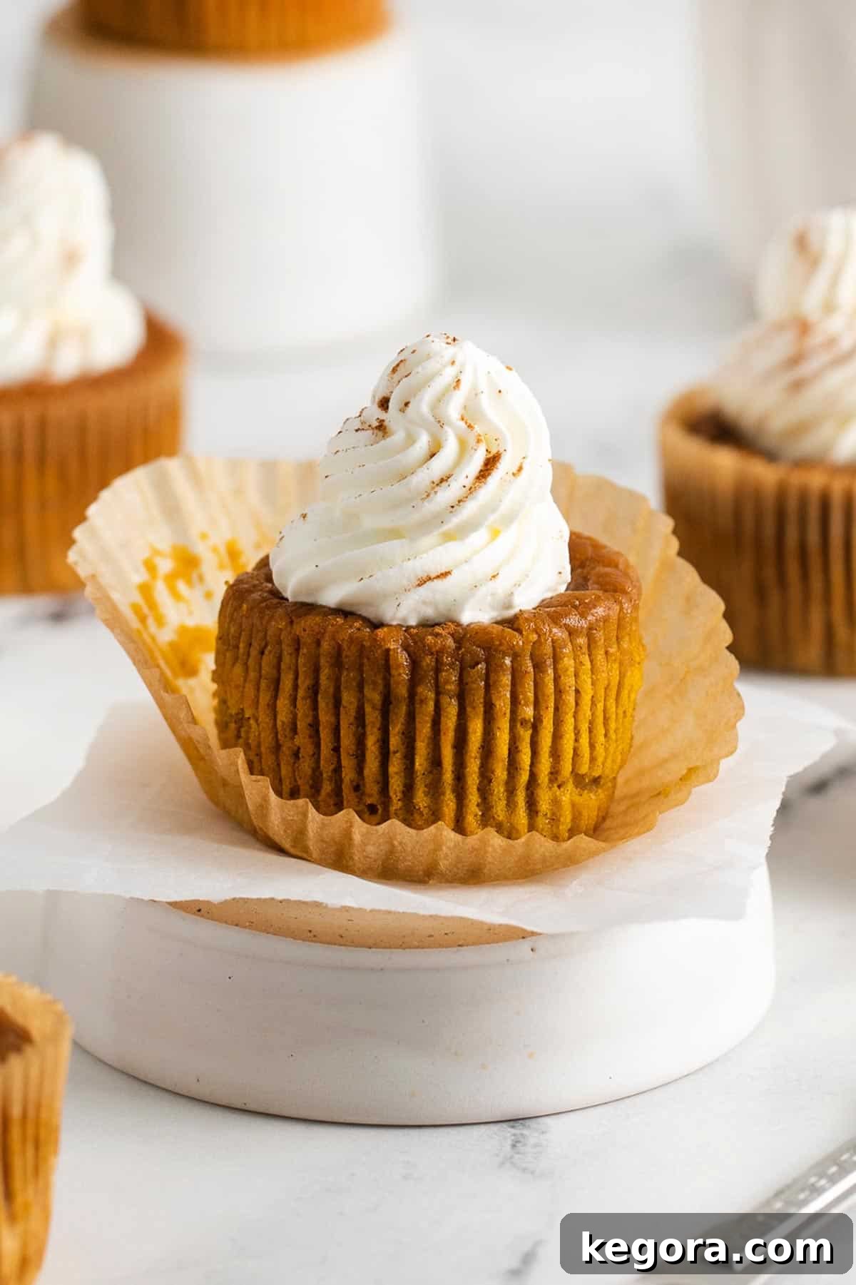 Close up of a fluffy gluten-free crustless pumpkin pie cupcake topped generously with whipped cream and a sprinkle of cinnamon on a pristine white surface, ready to be served.