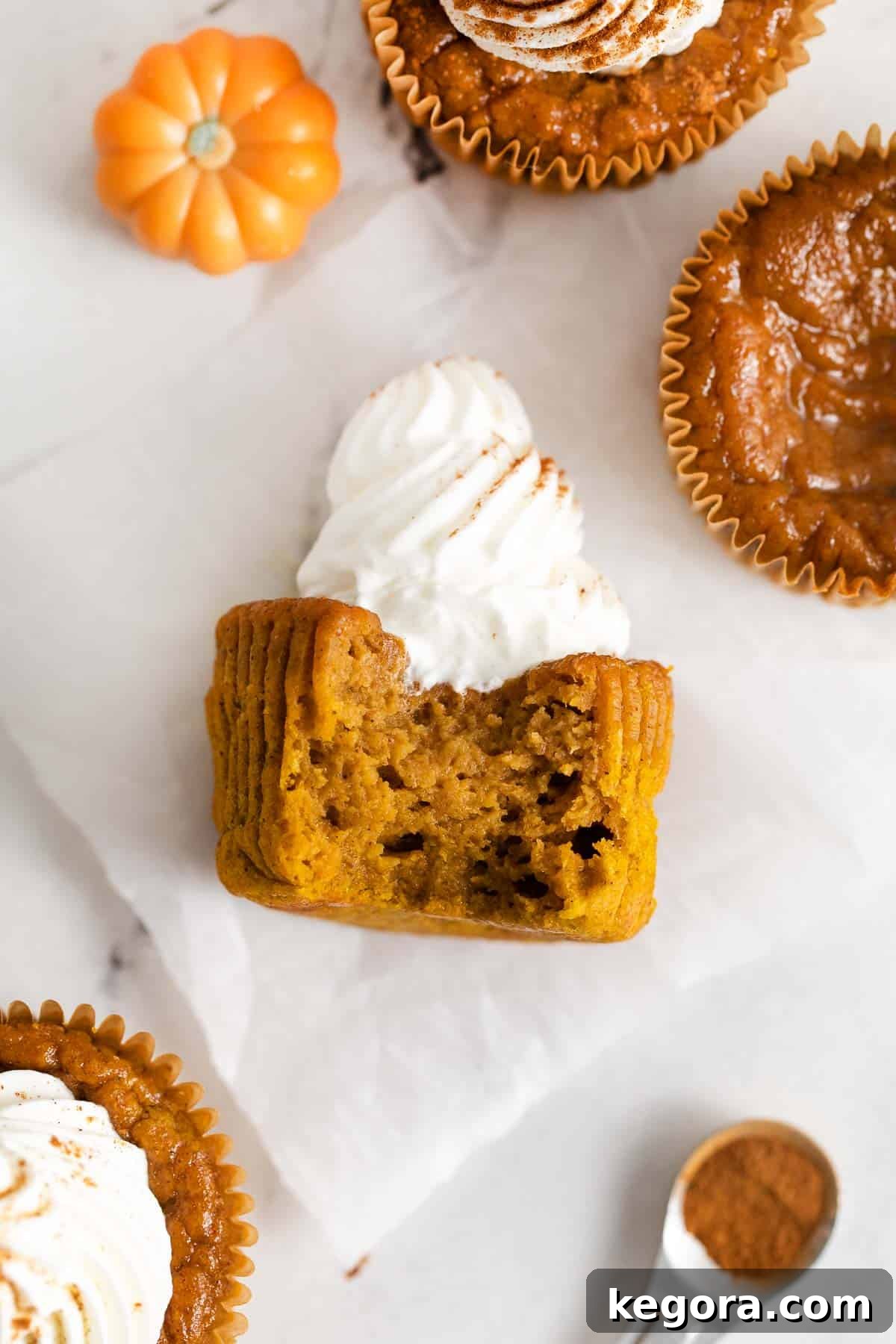 A close-up view of a gluten-free crustless pumpkin pie cupcake with a small bite taken out, revealing its smooth, custardy interior.