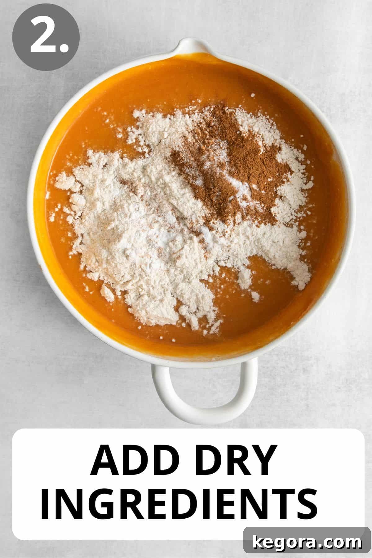 Dry ingredients, a blend of flour and spices, being carefully added to the vibrant orange wet pumpkin mixture in a white mixing bowl.
