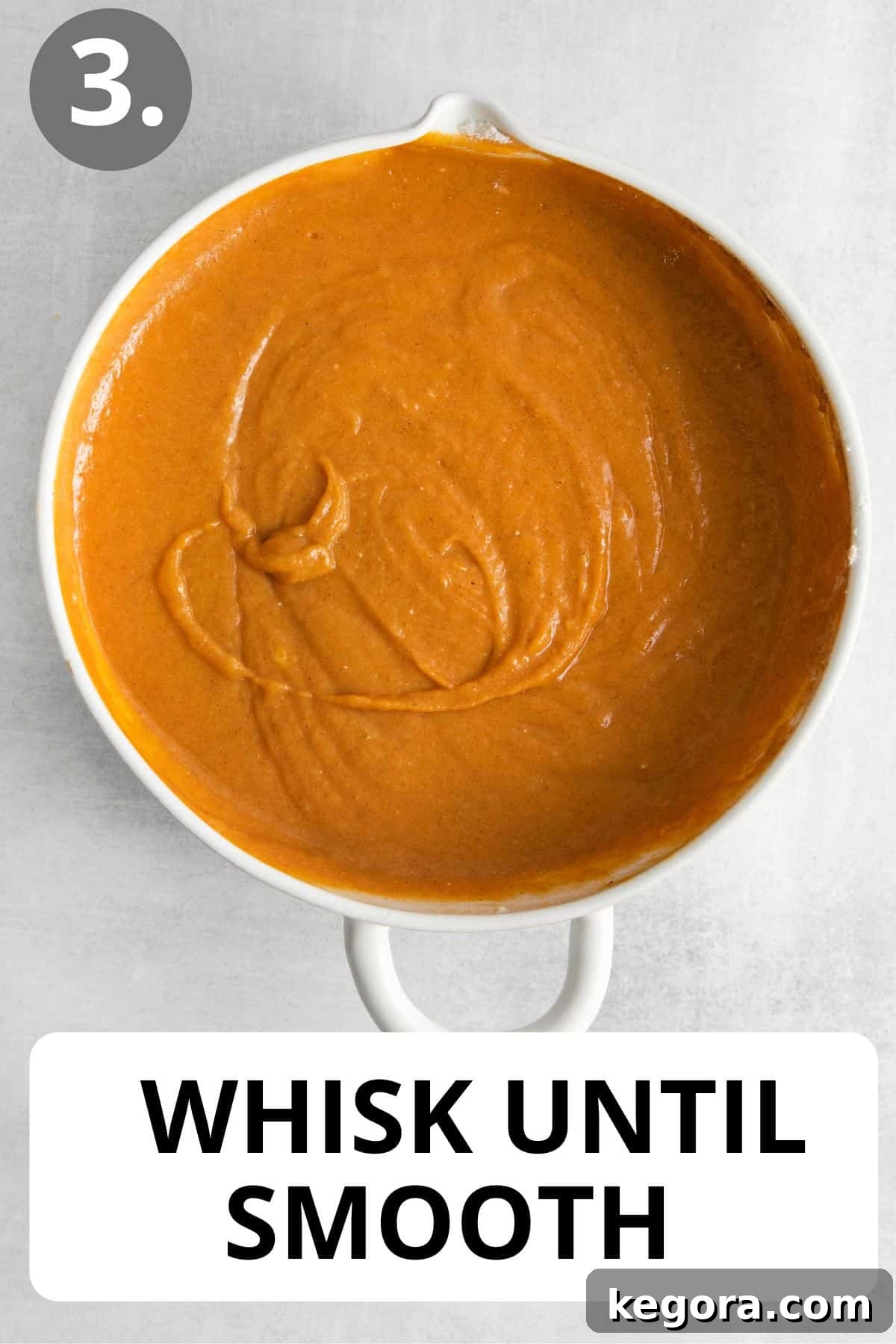 The fully mixed, smooth pumpkin pie filling, ready to be scooped, rests in a white bowl, showcasing its rich orange color.
