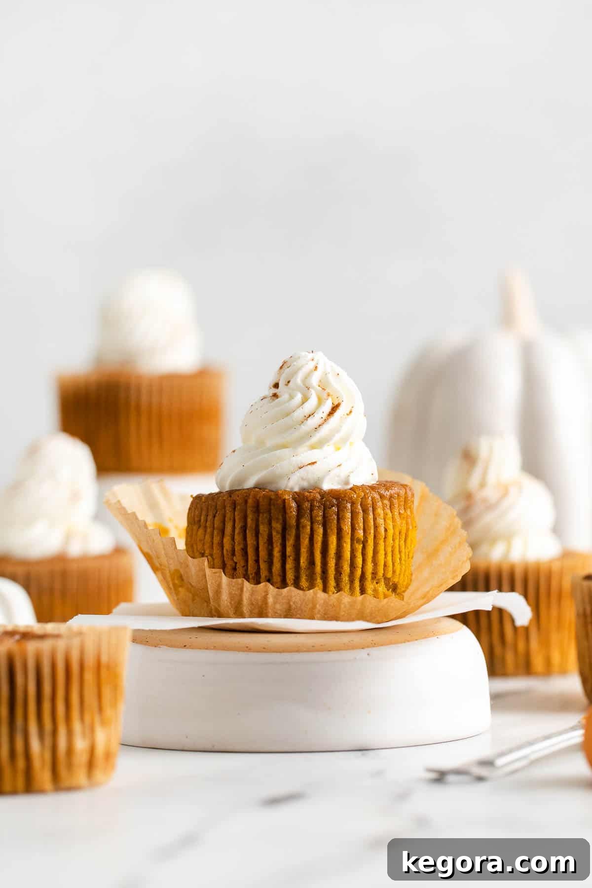 A perfectly baked crustless pumpkin pie cupcake, elegantly topped with whipped cream and a sprinkle of cinnamon, resting on a white surface, showcasing its delightful appeal.