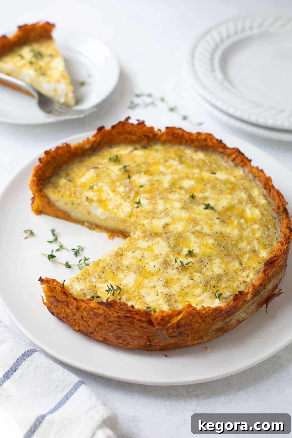 Golden Sweet Potato Quiche with Creamy Goat Cheese and Leeks 3 Sweet potato crust quiche on a white plate topped with fresh thyme, ready to be served