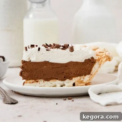 Side view of a perfect slice of chocolate angel pie on a white plate, highlighting the distinct layers of meringue, chocolate mousse, and whipped cream.