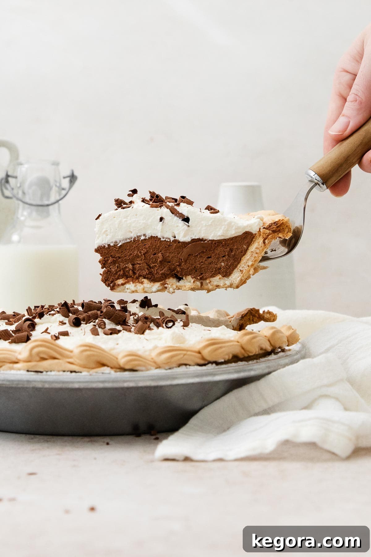 A hand gracefully raising a perfectly sliced piece of Chocolate Angel Pie from the pie dish with a serving spoon, showcasing its layered beauty.
